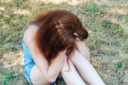 A young pretty girl with red hair is holding her head, it became bad on the street, very sad.の写真素材