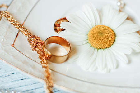 Delicate daisies close-up with gold jewelry. Chains, pendants, rings on a stand.の写真素材