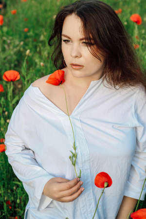 Attractive woman in a poppy field in summer in a white shirt.の写真素材