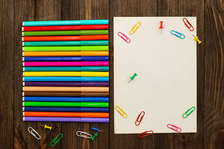 School creative flatley. On a wooden table are multi-colored felt-tip pens and a sheet with empty space for text.の写真素材