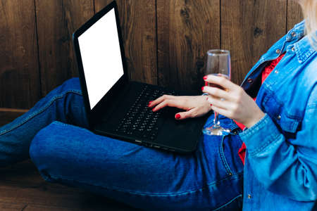 Girl with blond hair in denim clothes sits with a glass of champagne with a laptop.の写真素材