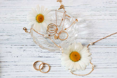 Delicate daisies close-up with gold jewelry. Chains, pendants, rings on a stand.の写真素材
