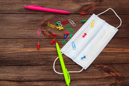 School creative flatley. Multi-colored paper clips with handles and a medical protective mask lie on a wooden table.の写真素材