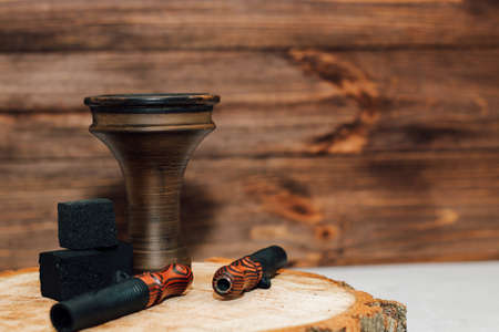 Clay bowl for hookah with coconut coals, wooden mouthpieces stands on a wooden background.の写真素材