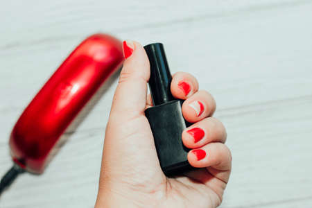 Spoiled cracked red nail polish on hands against the background of a gel polish dryer.の写真素材