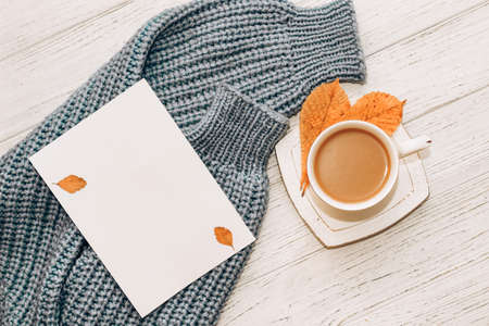 White cup with coffee with milk on the background of a knitted sweater and autumn leaves with a place for the text.の写真素材