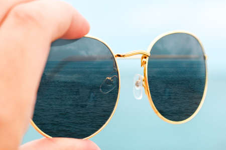 girl holding sunglasses in her hands on a background of blue sky in glasses displays the sea.の写真素材