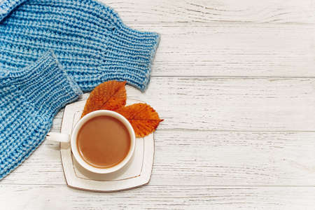 White cup with coffee with milk on the background of a knitted sweater and autumn leaves.の写真素材