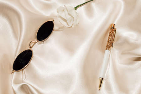 Glasses and a pen on a silk beige background, space for text.の写真素材