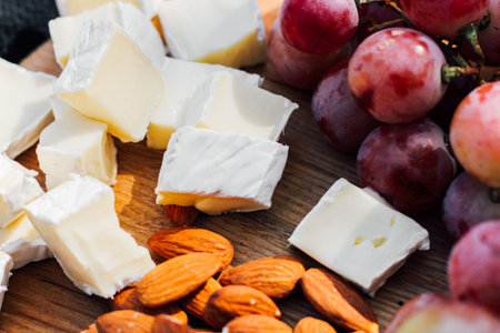 Wooden board with fruits, cheese, nuts, picnic snacks.