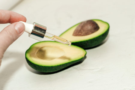 Green ripe avocado with face serum on a light background.