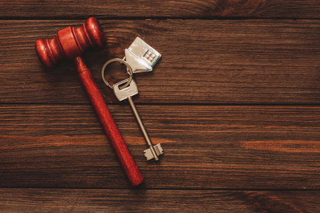 The key to the apartment with a keychain in the shape of a house on wooden background.の写真素材