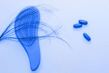 Plastic comb with fallen hair and pills on a wooden background.の写真素材