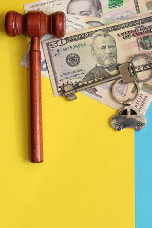 The key to the apartment with a keychain in the shape of a house on a blue yellow background, the colors of the flag of Ukraine, hryvnias and dollars, judge's hammer.の写真素材