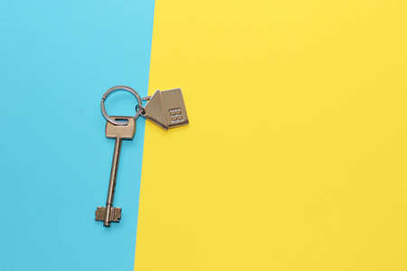 The key to the apartment with a keychain in the shape of a house on a cardboard blue yellow background, the colors of the flag of Ukraine.の写真素材
