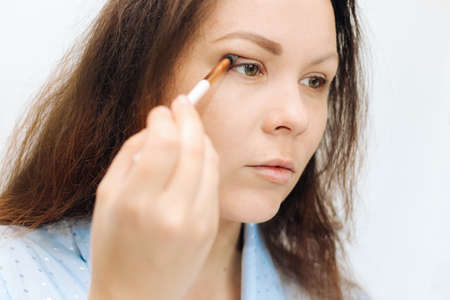 The girl paints her eyes with a brush with dry shadows, correcting the overhanging eyelid the shape of the eye.の写真素材