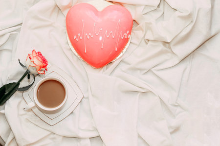 Pink tea rose with heart shaped pink mousse cake with a cup of coffee.の写真素材