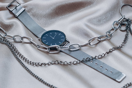 Stylish silver chain decorations for the neck and watch on a silk shiny background.の写真素材