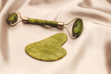 massage stone jade gouache scraper and facial roller on silk background.の写真素材