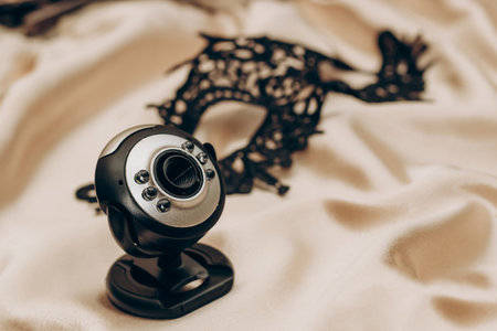 Sexy black lace stylish masquerade mask and webcam on golden silk sheet, web modeling concept.の写真素材