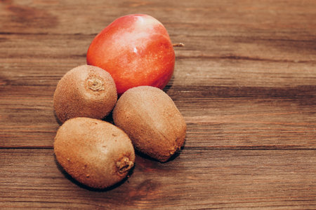 Fluffy fruits three kiwi and an apple lie on a wooden brown table.の写真素材