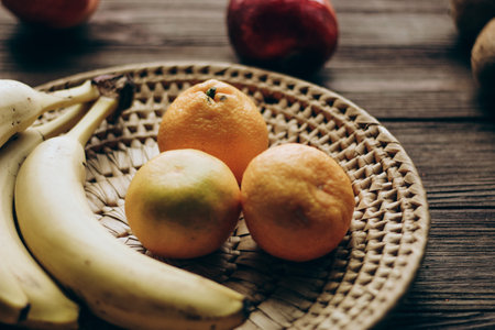 A wicker bowl with fruit stands on a wooden brown table.の写真素材