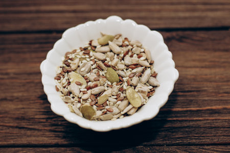 A mixture of sunflower, pumpkin and flax seeds in a bowl on a wooden table.の写真素材