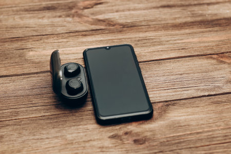 Wireless headphones in a black box on the table next to the phone.の写真素材