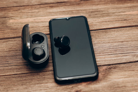 Wireless headphones in a black box on the table next to the phone.の写真素材