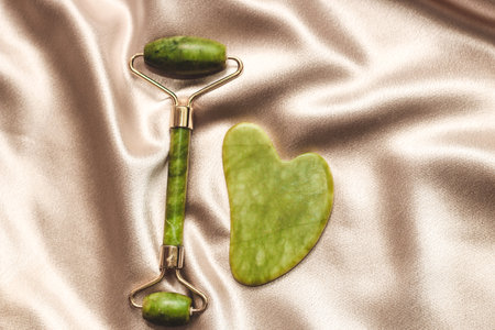 massage stone jade gouache scraper and facial roller on silk background.の写真素材