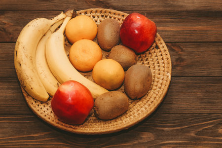 Fruit banana, kiwi, apple, tangerines lie in a wicker plate.の写真素材
