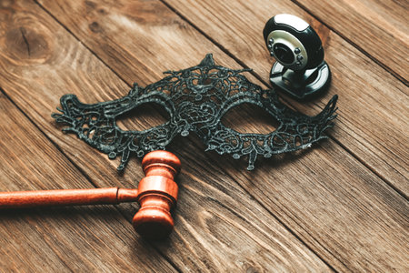 Black lace masquerade mask and webcam with judge hammer on table, legal web modeling concept.の写真素材