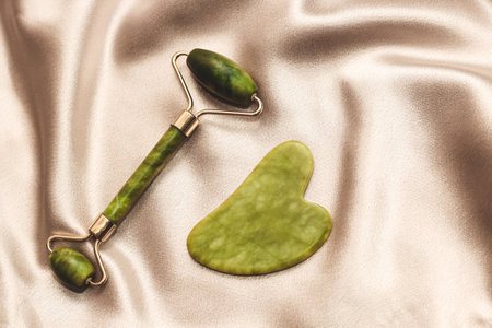 massage stone jade gouache scraper and facial roller on silk background.の写真素材