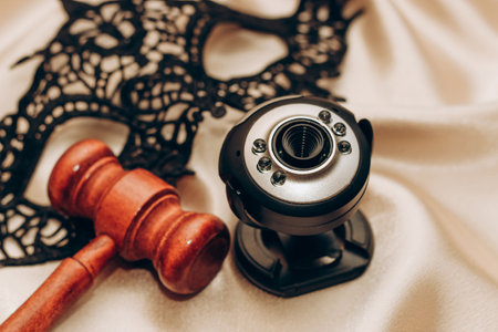 Black lace masquerade mask and webcam with judge hammer on sheet, legal web modeling concept.の写真素材