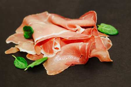 Pieces of dried pork jamon prosciutto on a black board.の写真素材