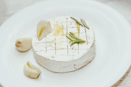 Round cheese in camembert mold with a sprig of rosemary, with garlic on the table.の写真素材