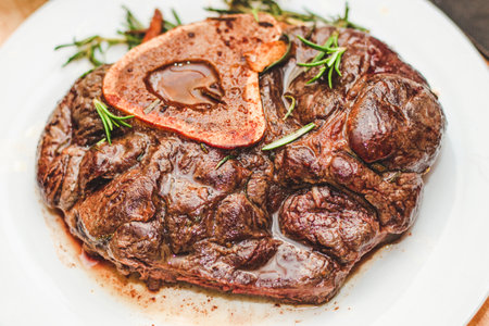 Cooked braised beef steak on the bone ossobuco with pepper, rosemary on the board.の写真素材