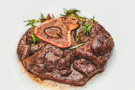 Cooked braised beef steak on the bone ossobuco with pepper, rosemary on the board.の写真素材