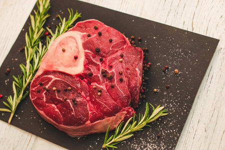 Fresh piece of meat large beef steak on the bone ossobuco with a sprig of rosemary on a black background.の写真素材
