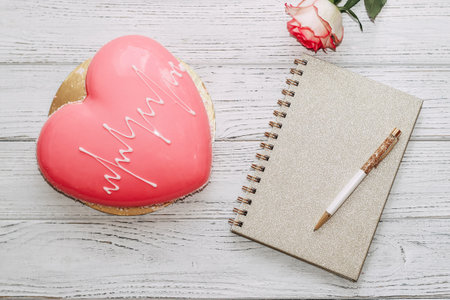 Heart shaped pink mousse cake on table with rose and notepad.の写真素材