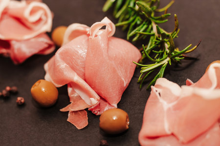 Pieces of dried pork jamon prosciutto with olives on a black board.の写真素材