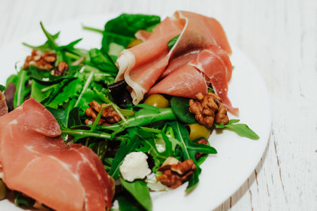 Salad with herbs, arugula, prosciutto, cheese, green olives and nuts.の写真素材