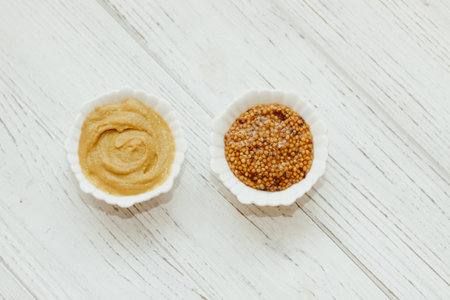 Mustard sauce and grain mustard in a white bowl on a white table.の写真素材