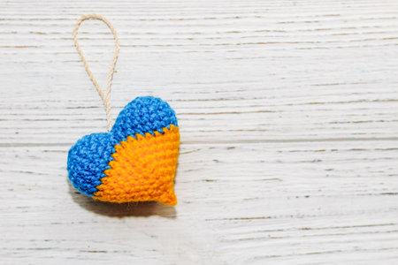 Knitted toy in the shape of a heart in the colors of the Ukrainian flag, blue and yellow threads.の写真素材