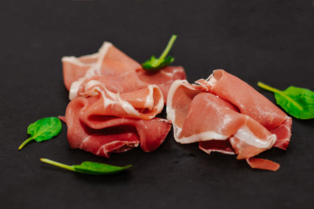 Pieces of dried pork jamon prosciutto on a black board.の写真素材