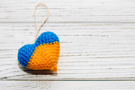 Knitted toy in the shape of a heart in the colors of the Ukrainian flag, blue and yellow threads.の写真素材