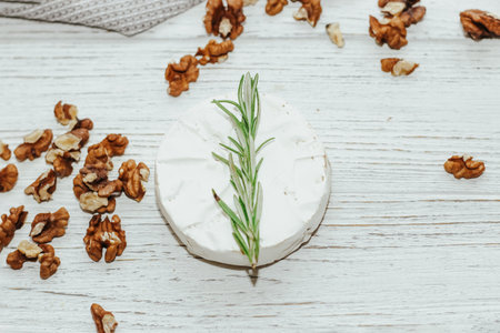 Round cheese in camembert mold with a sprig of rosemary on the table.の写真素材