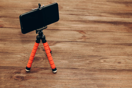 The phone stands on a manual monopod tripod for the camera on a wooden table..の写真素材