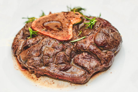 Cooked braised beef steak on the bone ossobuco with pepper, rosemary on the board.の写真素材