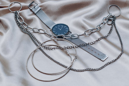 Stylish silver chain decorations for the neck and watch on a silk shiny background.の写真素材
